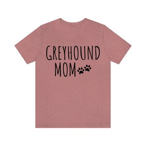 May include: A heather pink t-shirt with the text "Greyhound Mom" and two black paw prints.