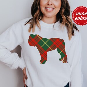 May include: White sweatshirt featuring a red, green, and yellow plaid bulldog silhouette. The sweatshirt has a crew neck and long sleeves. A red circle with the words "more colors" is in the upper right corner.