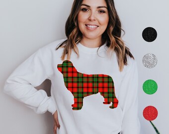 Puede incluir: Sudadera blanca con una silueta de perro a cuadros en rojo, verde y negro. El diseño es un patrón de cuadros festivo. La sudadera tiene cuello redondo y mangas largas. El fondo es blanco liso.
