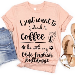 May include: A peach-colored t-shirt with the text "I just want to drink coffee & be with my Olde English Bulldogge" in black. The shirt has a coffee cup graphic and paw prints.
