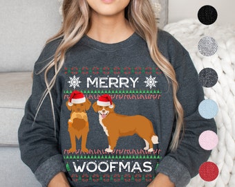 Peut inclure: Un sweat-shirt gris foncé avec un motif de Noël représentant deux Nova Scotia Duck Tolling Retrievers portant des bonnets de Père Noël. Le texte "Merry Woofmas" est imprimé sur le sweat-shirt.
