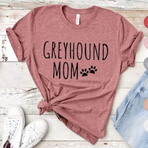 May include: A heather pink t-shirt with the text "Greyhound Mom" and two paw prints in black.