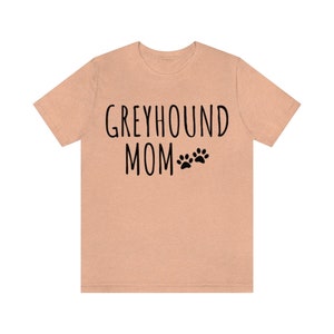 May include: A peach-colored t-shirt with the text "Greyhound Mom" and two paw prints in black.