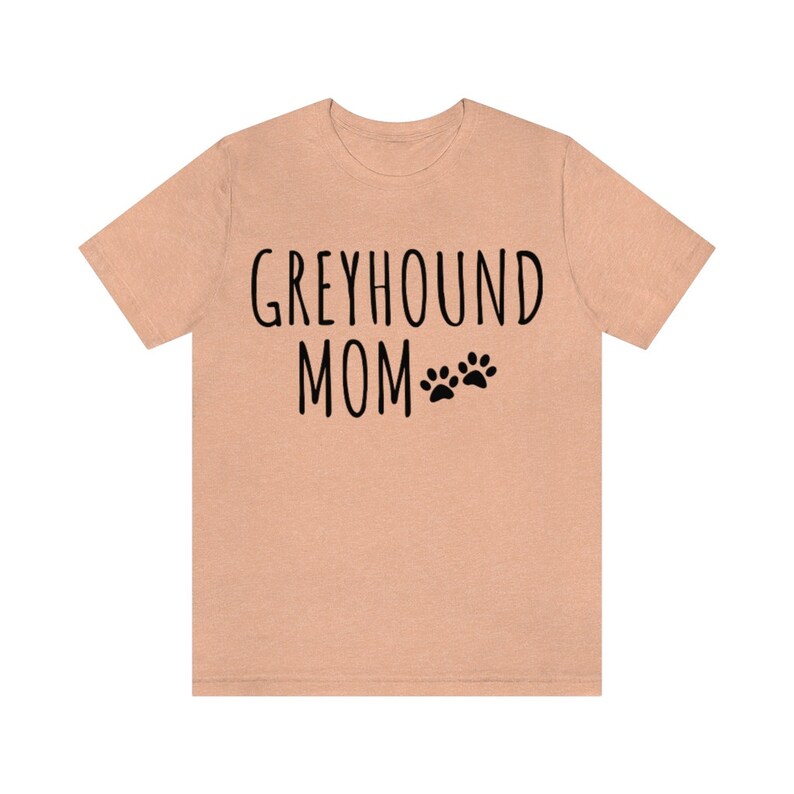 May include: A peach-colored t-shirt with the text "Greyhound Mom" and two paw prints in black.