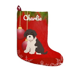 May include: Red Christmas stocking with a white snowflake design and the name "Charlie" in white script. The stocking features a black and white dog illustration, two red ornaments, and green pine needles.