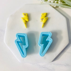 May include: Two pairs of lightning bolt shaped earrings. One pair is yellow with gold flecks and the other pair is light blue.