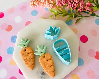 May include: Two orange carrot-shaped polymer clay earrings with green tops, and two blue plastic cookie cutters in the shape of a carrot and a carrot top.