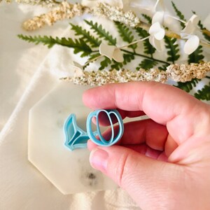 May include: A light blue plastic cookie cutter shaped like a peach with a leaf.