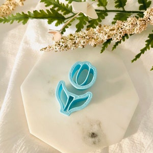 May include: A light blue plastic tulip cookie cutter on a white marble surface.