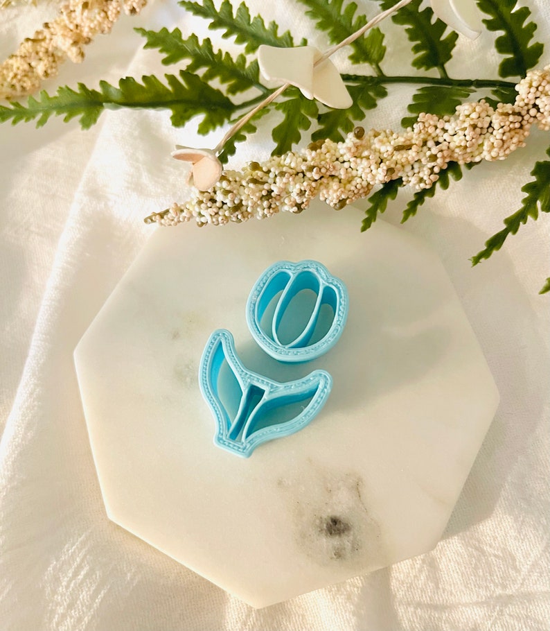 May include: A light blue plastic tulip cookie cutter on a white marble surface.