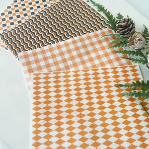 Op de afbeelding: Vier vellen decoratief inpakpapier met verschillende patronen. De patronen zijn zwart-oranje geruit, zwart-oranje golvende lijnen, wit-oranje geruit en wit-oranje ruitvormig.