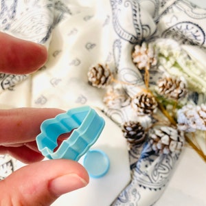 May include: A light blue plastic cookie cutter shaped like a cloud. The cutter has a wavy edge and is held in a hand.