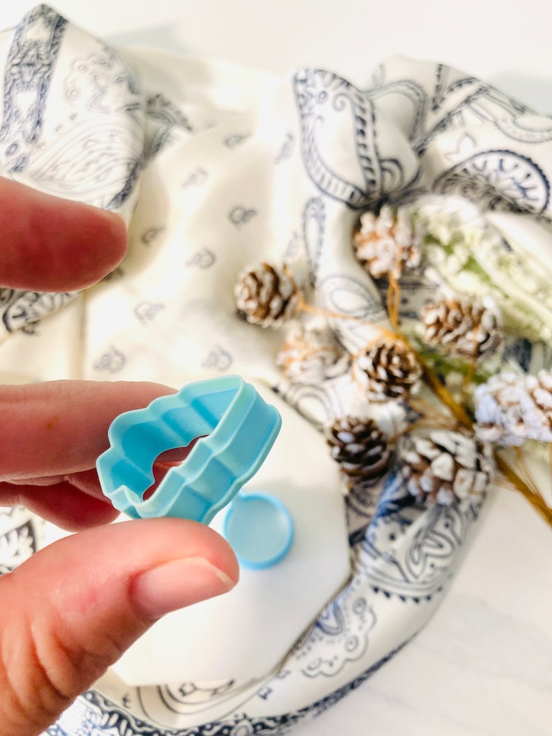 May include: A light blue plastic cookie cutter shaped like a cloud. The cutter has a wavy edge and is held in a hand.