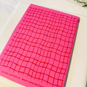 Może przedstawiać: R&oacute;żowa silikonowa mata do pieczenia z falistym wzorem kratki. Mata ma nadrukowany tekst "SO CAL CUTTER CO: WAVY GRID PATTERN" na spodzie.