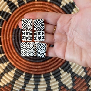 Puede incluir: Un par de pendientes cuadrados con patrones geom&eacute;tricos en blanco y negro. Los pendientes son de forma cuadrada y tienen un fondo blanco con dise&ntilde;os geom&eacute;tricos negros.
