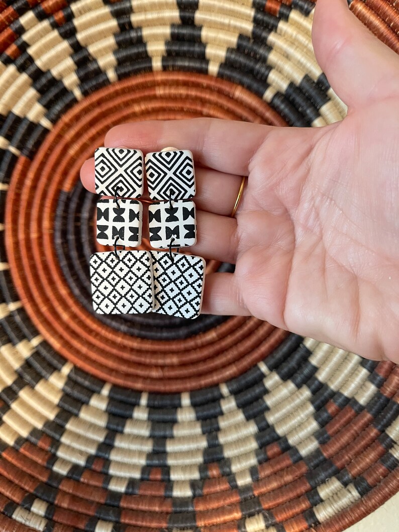 Puede incluir: Un par de pendientes cuadrados con patrones geom&eacute;tricos en blanco y negro. Los pendientes son de forma cuadrada y tienen un fondo blanco con dise&ntilde;os geom&eacute;tricos negros.
