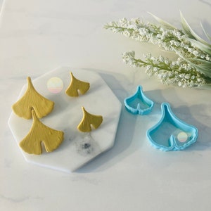 May include: Two sets of ginkgo leaf earrings, one set is blue and the other is yellow. The blue set is a pair of silicone molds for making the earrings. The yellow set is a pair of finished earrings.