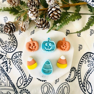 Könnte beinhalten: Ein Set mit fünf Halloween-förmigen Ausstechern. Die Ausstecher sind aus blauem und orangefarbenem Kunststoff und haben Kürbis- und Mais-Designs.