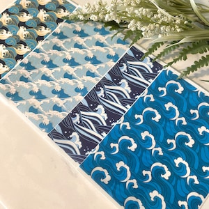 May include: Four different patterned sheets of paper featuring blue and white waves. The patterns are all different, but they all have a similar theme of water and waves.