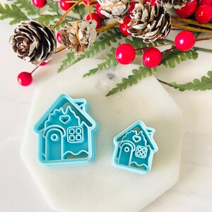 May include: Two blue plastic gingerbread house cookie cutters, one larger than the other, on a white marble surface.