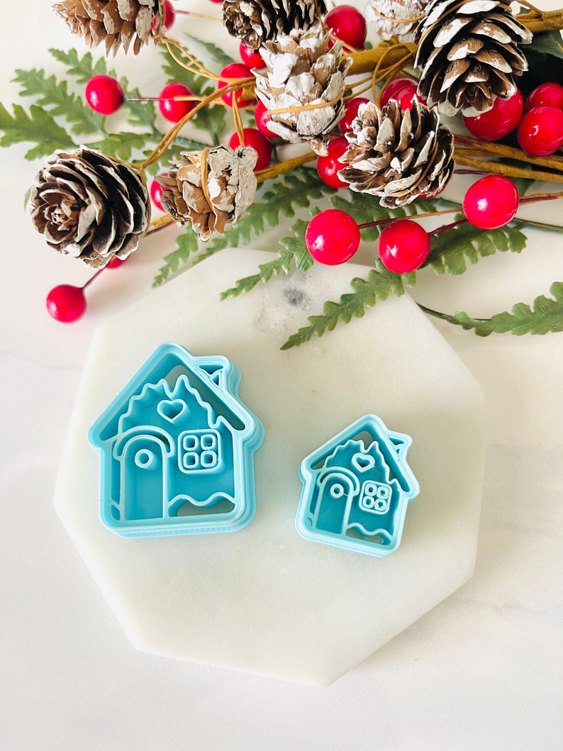 May include: Two blue plastic gingerbread house cookie cutters, one larger than the other, on a white marble surface.