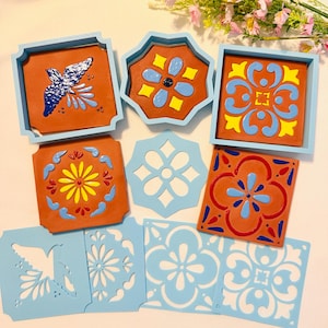 May include: A collection of terracotta tiles featuring painted floral and bird motifs in blue, yellow, and red, accompanied by light blue wooden frames and matching stencils. The set includes square and octagonal shapes with intricate patterns.