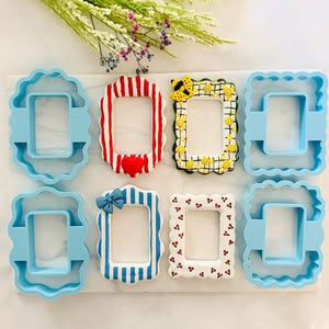 May include: Four light blue plastic rectangular cookie cutters with scalloped edges and four decorated rectangular frames. The frames feature red and white stripes with a heart, a yellow bee and flower pattern, blue stripes with a bow, and cherries.
