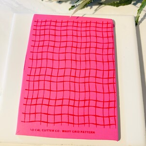 Może przedstawiać: R&oacute;żowa i czerwona mata do cięcia z falistym wzorem siatki z nadrukowanym tekstem "SO CAL CUTTER CO: WAVY GRID PATTERN" na dole.