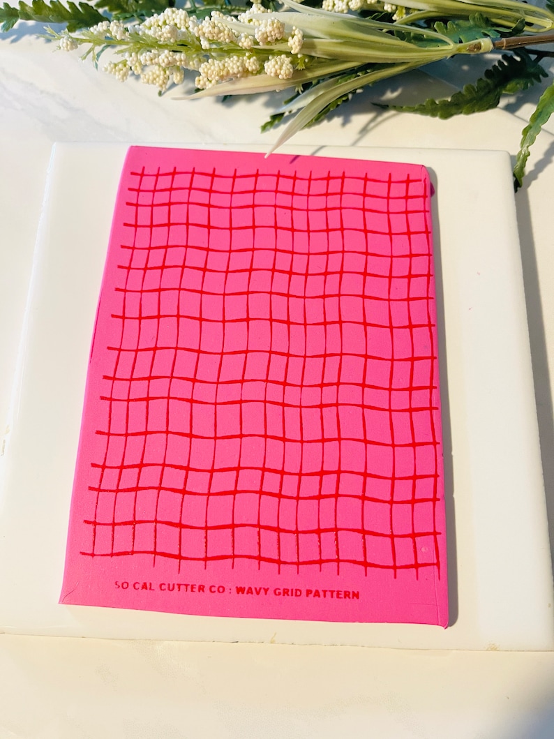 Może przedstawiać: R&oacute;żowa i czerwona mata do cięcia z falistym wzorem siatki z nadrukowanym tekstem "SO CAL CUTTER CO: WAVY GRID PATTERN" na dole.