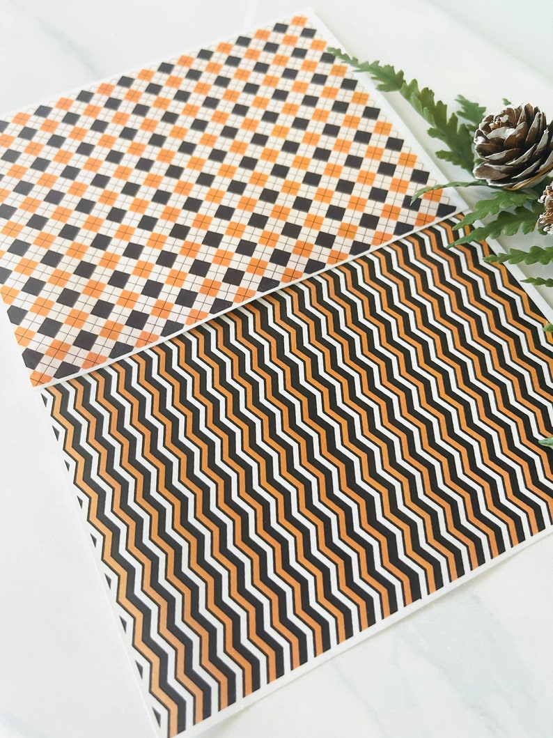 Op de afbeelding: Twee vellen met een geometrisch patroon in zwart, wit en oranje. Het bovenste vel heeft een geruit patroon en het onderste vel heeft een zigzagpatroon.