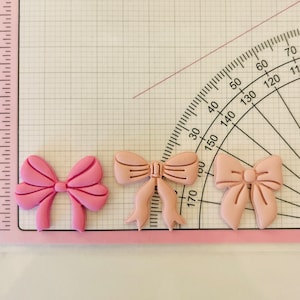May include: Three pink and light pink bows made of felt. The bows are different sizes and shapes.