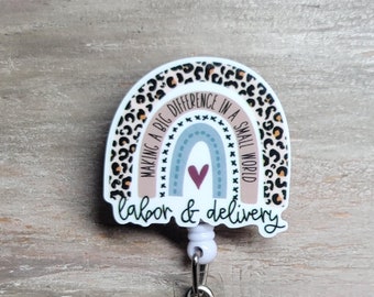 May include: A white plastic badge holder with a rainbow design featuring a leopard print pattern. The rainbow has a heart in the center and the text "Making a big difference in a small world labor & delivery".