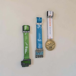 Peut inclure: Trois médailles de course avec rubans. Le ruban vert porte un pendentif Cannock Chase 10K 2017 et une étiquette 00:56:38. Le ruban bleu porte un pendentif Stafford Half 2018 et une étiquette 01:59:16. Le ruban blanc porte un pendentif Greater Manchester Marathon et une étiquette 05:29:35.
