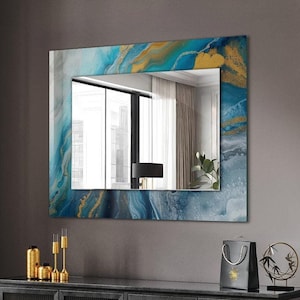 May include: A black wooden table with a stack of books and a candle holder. A large mirror with a blue and gold abstract design hangs on the wall above a black cabinet.