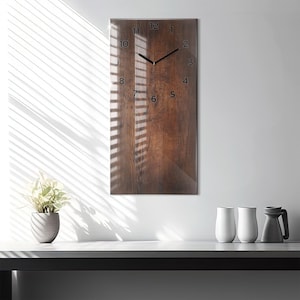 May include: A rectangular wall clock with a wood-grain design. The clock face features black numerals and hands against a brown background. The clock is mounted on a white wall, with light and shadow patterns.