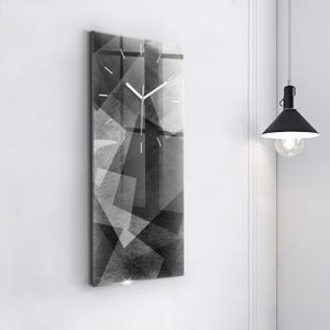 Puede incluir: Un reloj de pared rectangular con un diseño moderno. La esfera del reloj presenta un patrón geométrico en blanco y negro. Las manecillas del reloj son blancas. El reloj está montado en una pared blanca.