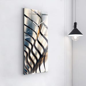 May include: A rectangular wall clock with a contemporary design. The clock face has a wavy pattern in silver, gold, and black. The clock hands are silver. The clock is mounted on a white wall.