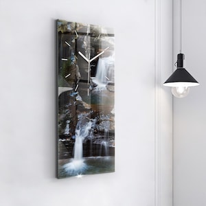 May include: A rectangular wall clock with a waterfall scene. The clock face features white hands and minimalist hour markers. The image depicts a cascading waterfall with rocks and greenery, creating a serene and natural aesthetic.