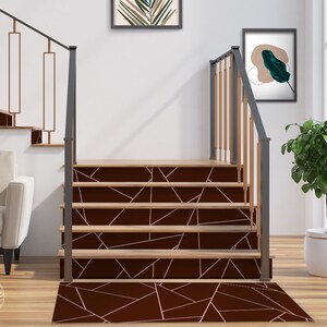 May include: A set of brown stair treads with a geometric pattern of thin gold lines. The treads are installed on a wooden staircase with a black metal railing.