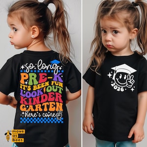 Könnte beinhalten: Schwarze Kinder-T-Shirts mit Designs zum Thema Abschluss. Ein Shirt zeigt den Text: "So long Pre-K, It's been fun, look out Kinder Garten, here I come." Das andere Shirt hat ein Smiley-Gesicht mit einem Abschluss-Hut und dem Jahr "2026."