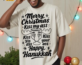 May include: Off-white t-shirt with a humorous graphic. The black text reads "Merry Christmas Kiss my ass" and "Happy Hanukkah". The graphic includes a cartoon face with antlers. The shirt is a casual, oversized fit.