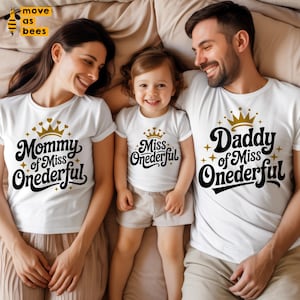 May include: Three white t-shirts with matching text and graphics. The shirts read "Mommy of Miss Onerderful", "Miss Onerderful", and "Daddy of Miss Onerderful". Each shirt has a gold crown graphic. The family is smiling.