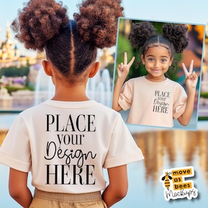 Puede incluir: Una persona joven lleva una camiseta blanca con el texto "PLACE YOUR DESIGN HERE" impreso en la parte delantera. La persona está de pie frente a un cuerpo de agua con un fondo borroso.