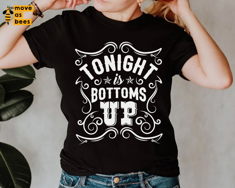 May include: Black t-shirt with a white graphic design that says "Tonight is Bottoms Up" in a vintage style font.