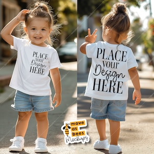 May include: White toddler t-shirt mockup with the text "PLACE YOUR DESIGN HERE" on the front and back. The shirt is being worn by a child standing on a sidewalk.