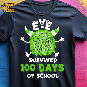 May include: Dark navy blue t-shirt with a green monster graphic. The monster has white arms and a green body covered in dark green spots. The text "EYE SURVIVED 100 DAYS OF SCHOOL" is in white and green.