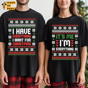 May include: Black t-shirts with Christmas-themed text. One shirt reads "I HAVE EVERYTHING I WANT FOR CHRISTMAS" in white, green, and red. The other shirt says "IT'S ME I'M EVERYTHING" in the same colors. Both shirts have a snowflake pattern.