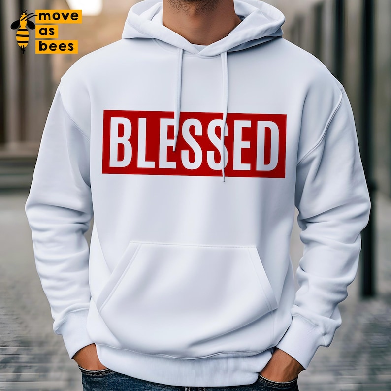 May include: White hoodie featuring the word "BLESSED" in white block letters within a red rectangle across the chest. The hoodie has a front pocket and a drawstring hood. The hoodie is white.