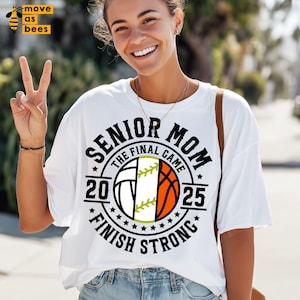 May include: White t-shirt with a graphic that says "SENIOR MOM THE FINAL GAME 2025 FINISH STRONG". The graphic features a split design with a volleyball, softball, and basketball. The shirt is a casual style.