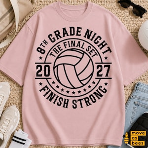 May include: A light pink short-sleeved t-shirt featuring a black graphic design of a volleyball. The text reads 8TH GRADE NIGHT, THE FINAL SET, 2027, and FINISH STRONG, arranged in a circular pattern around the central volleyball illustration.